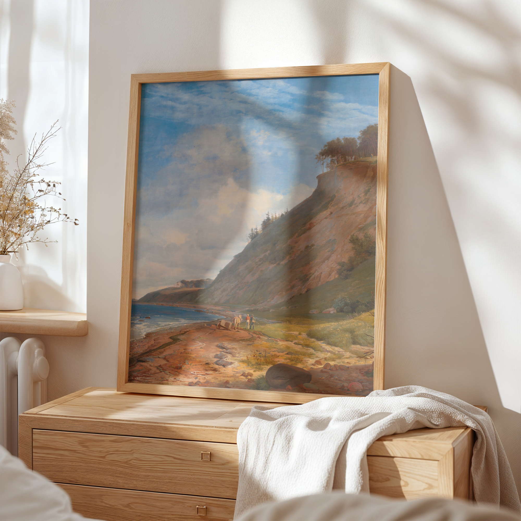 Framed landscape painting on a wall above a wooden dresser.
