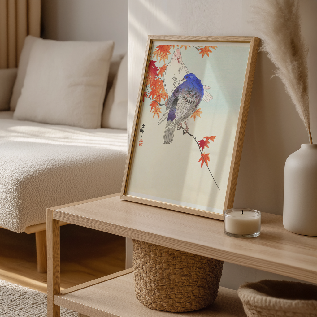 Framed artwork of a bird on a branch with autumn leaves on a wooden coffee table.