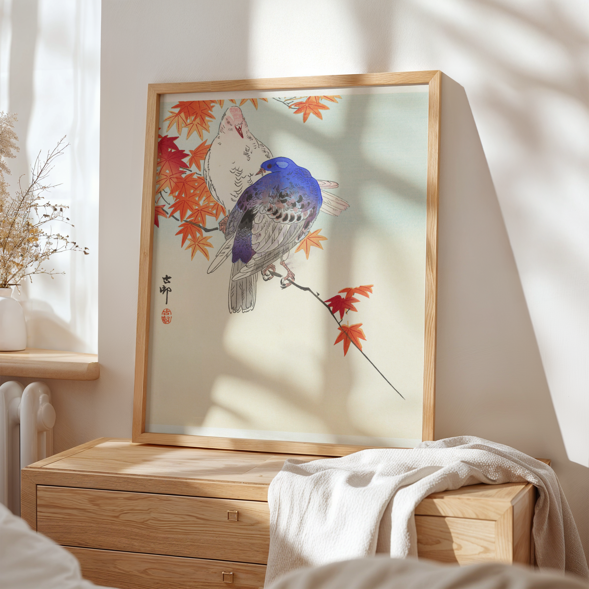 Framed artwork of a bird on a branch with autumn leaves in a room with a wooden dresser.